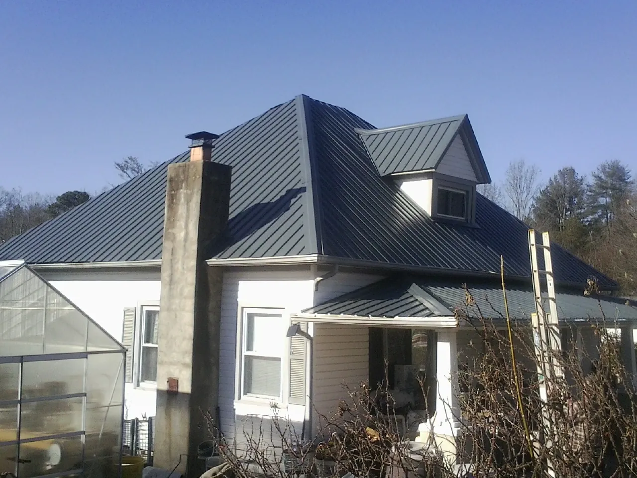 Dark blue standing seam metal roof on a white farmhouse with dormer — Slate & Tile Roof Repair by Roofing Brothers in Hartsdale