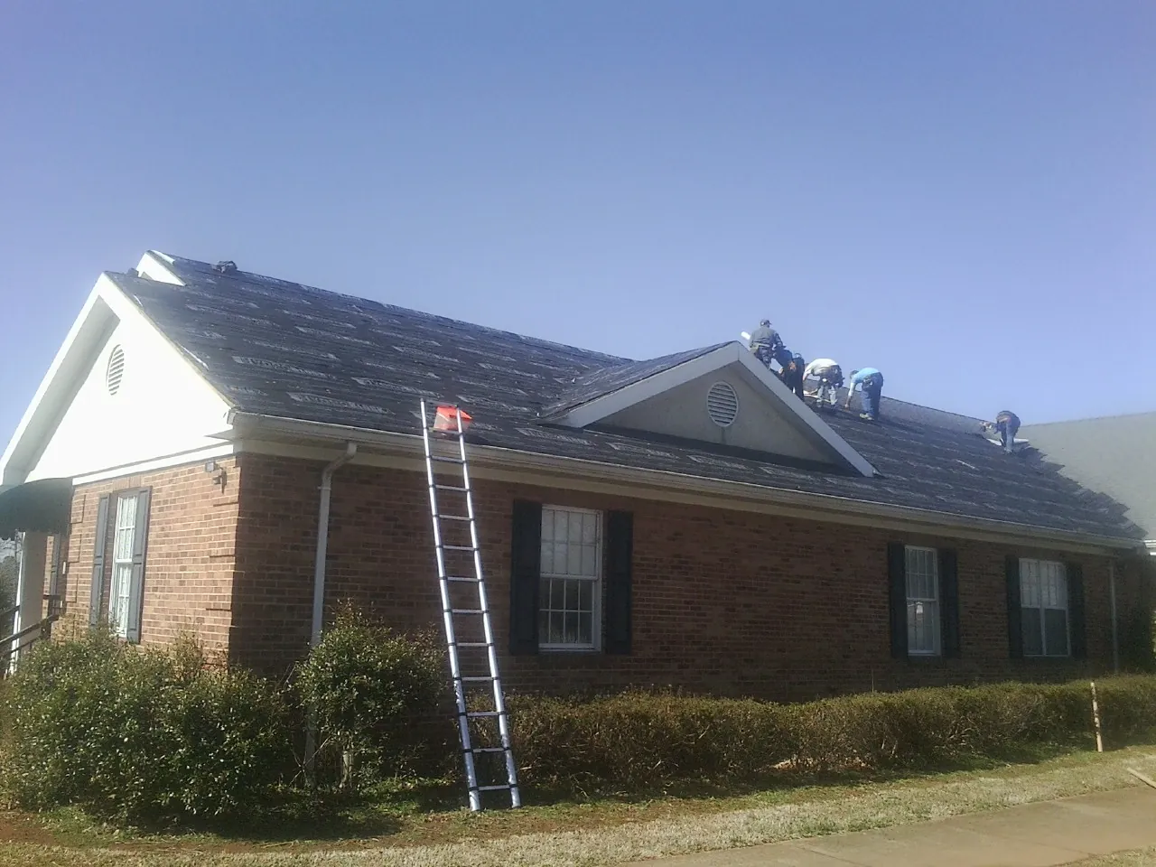 Crew tearing shingles off a brick ranch roof with a ladder set — Metal Roof Repair work by our crew in Hartsdale
