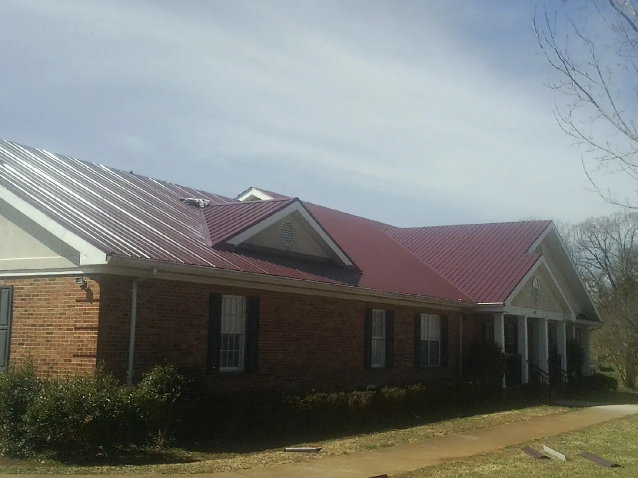 Red metal roof with gabled entries on a long brick building, from a Hail Damage Roof Repair job in Hartsdale