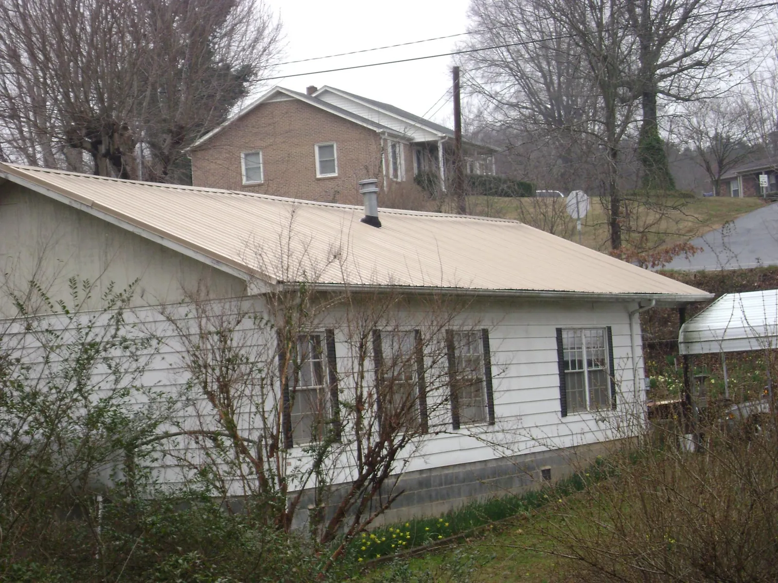 Tan metal roof on a white sided house set into a hillside — Commercial Roofing by Roofing Brothers in Hartsdale