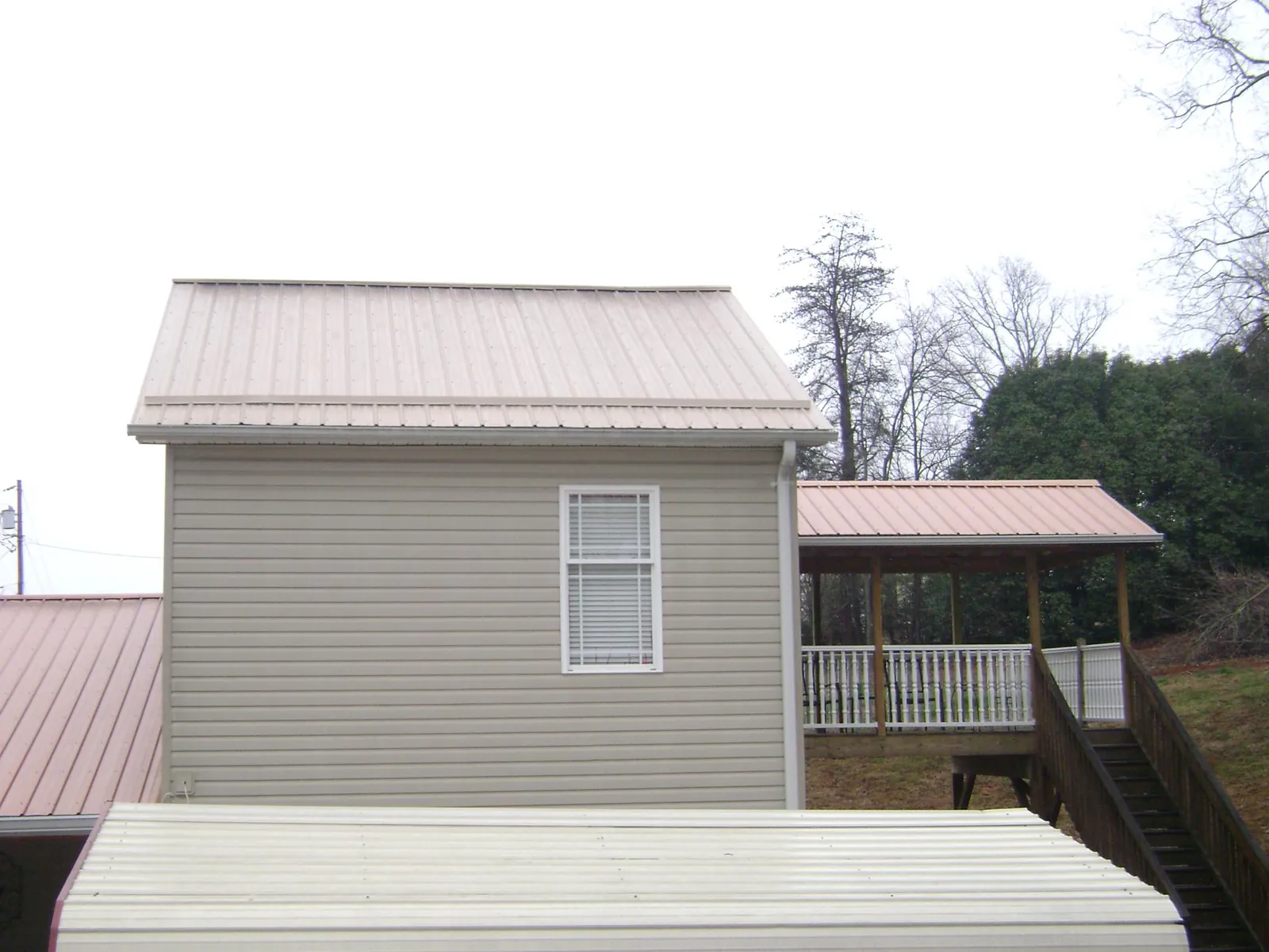 Tan metal roofs on a two story addition and attached porch, from a Roof Replacement job in Hartsdale